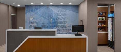 A reception desk with a digital screen, a wall with text, and a snack bar.