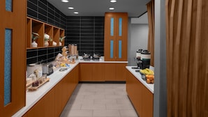 A modern kitchen with wooden cabinets, a white countertop, and a black backsplash. There are various kitchen appliances and a coffee machine on the counter.