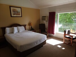Habitación de hotel con cama, una silla, escritorio, lámpara, teléfono y ventana con cortinas.