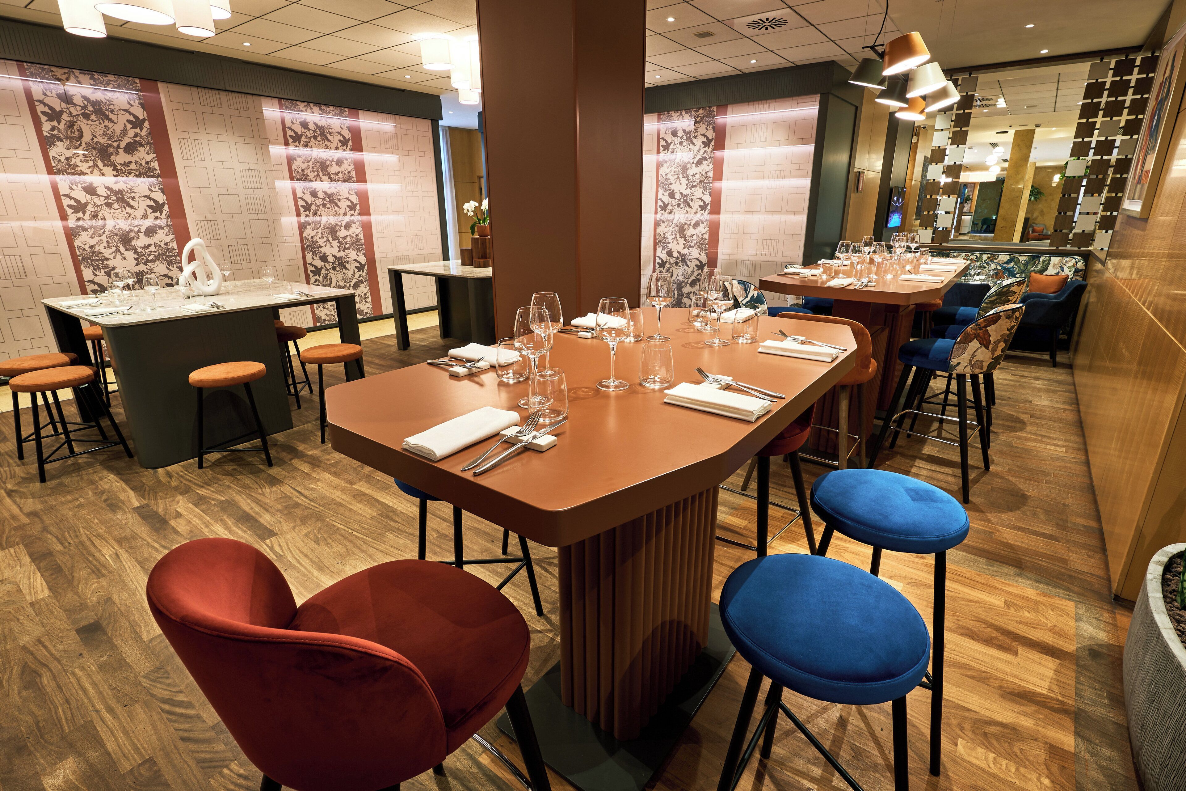A restaurant with a long table set for dining, red and blue chairs, and a bar area with stools.