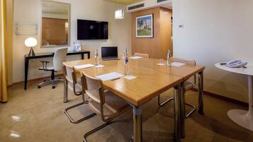 Une salle de conférence avec une table en bois, des chaises, un ordinateur portable, un téléphone et un téléviseur fixé au mur.