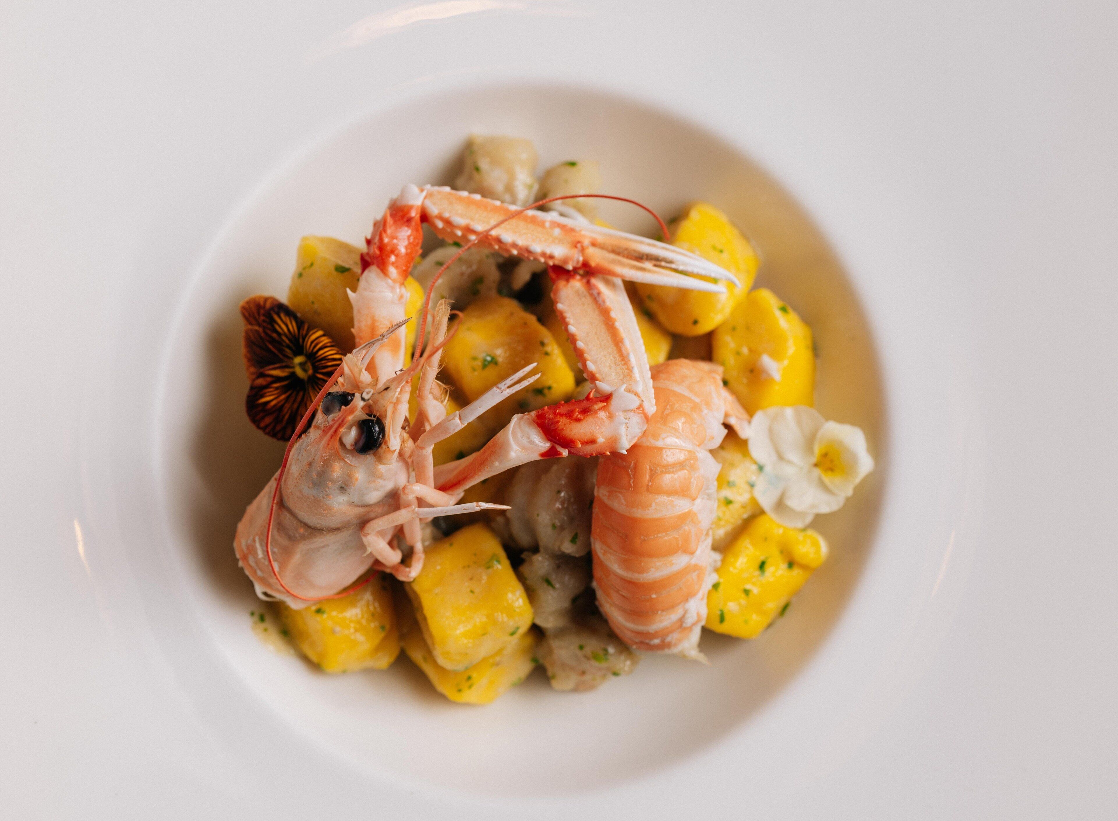 A plate of food with shrimp and yellow cubes, possibly mango.