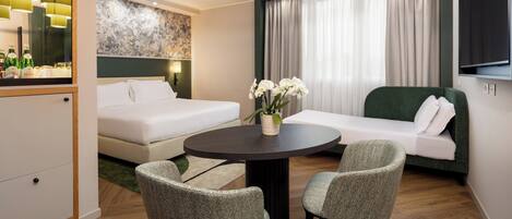 Una habitación de hotel moderna con cama, sofá, mesa de comedor con dos sillas, televisor y un elemento decorativo en la pared.