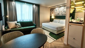 Una habitación de hotel moderna con un sofá verde, una cama, una mesa de comedor y un minibar.
