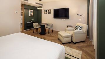 A hotel room with a bed, a desk with two chairs, a television, and a sofa.