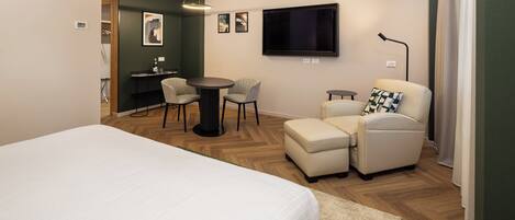 A hotel room with a bed, a desk with two chairs, a television, and a sofa.