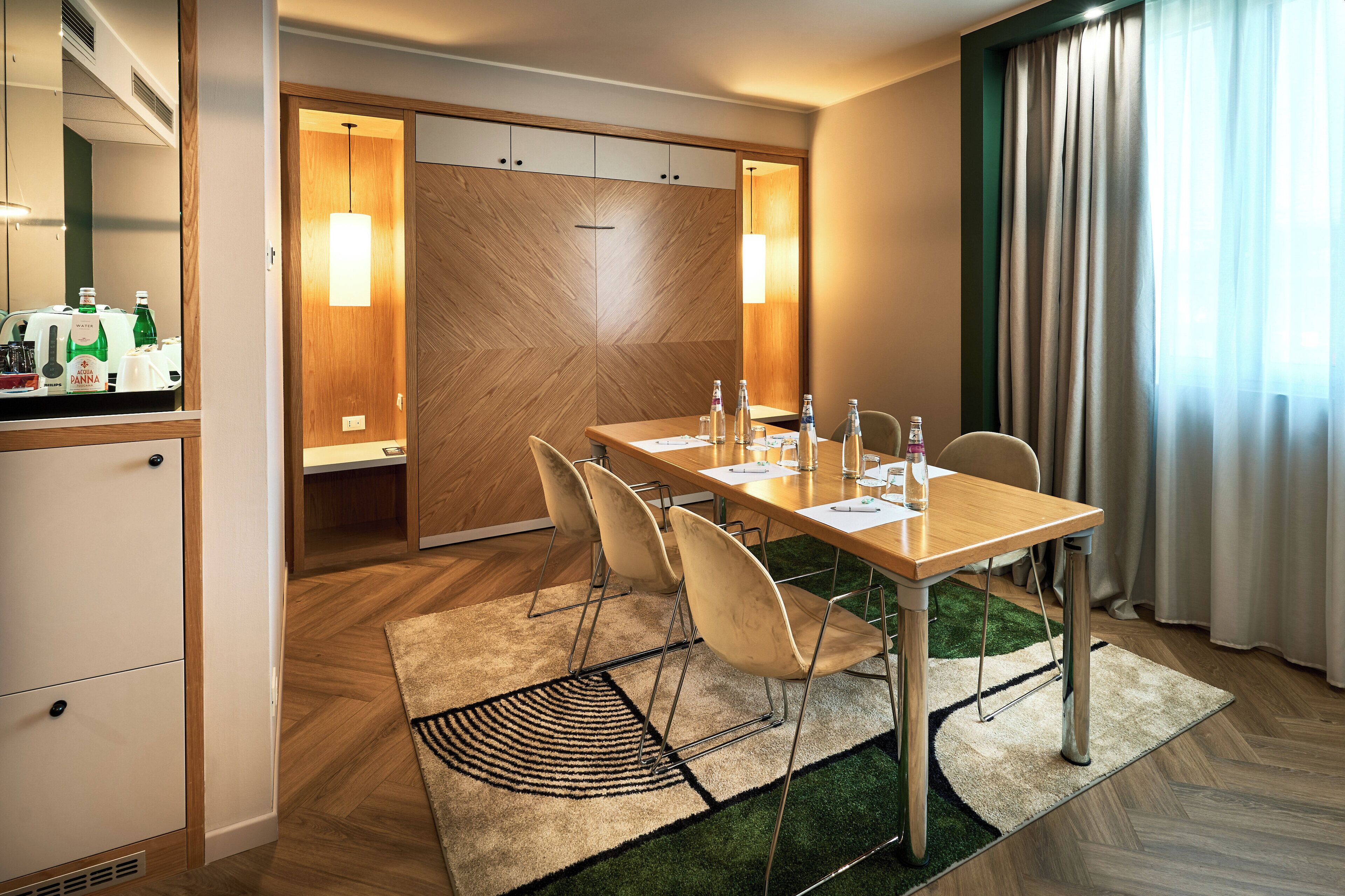 A hotel room with a dining table, chairs, a minibar, and a large window with curtains.
