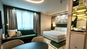 Una habitación de hotel moderna con un sofá verde, una cama, una mesa de comedor y un minibar.