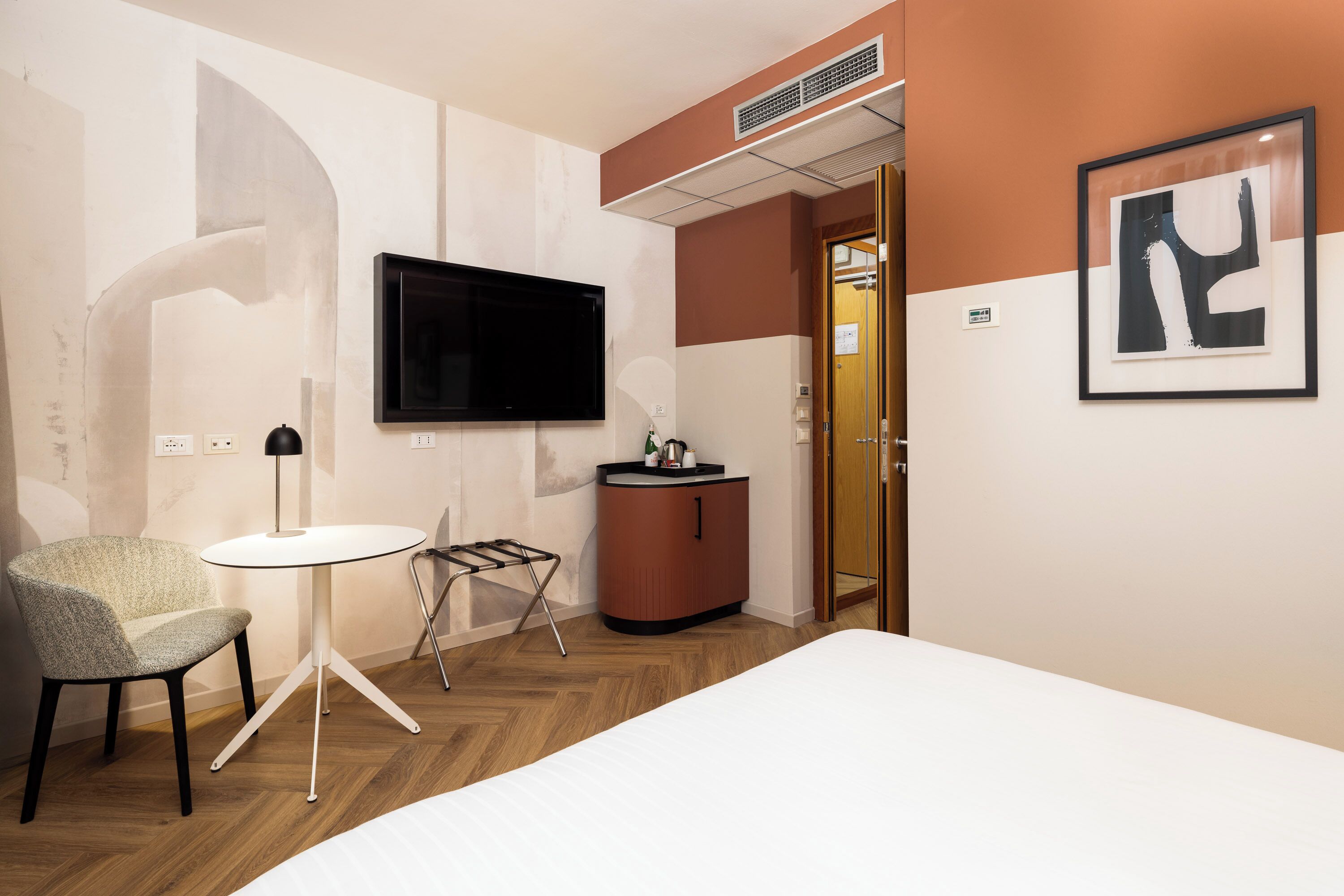 Habitación de hotel con una cama, televisor montado en la pared, una mesita, una silla y un armario.