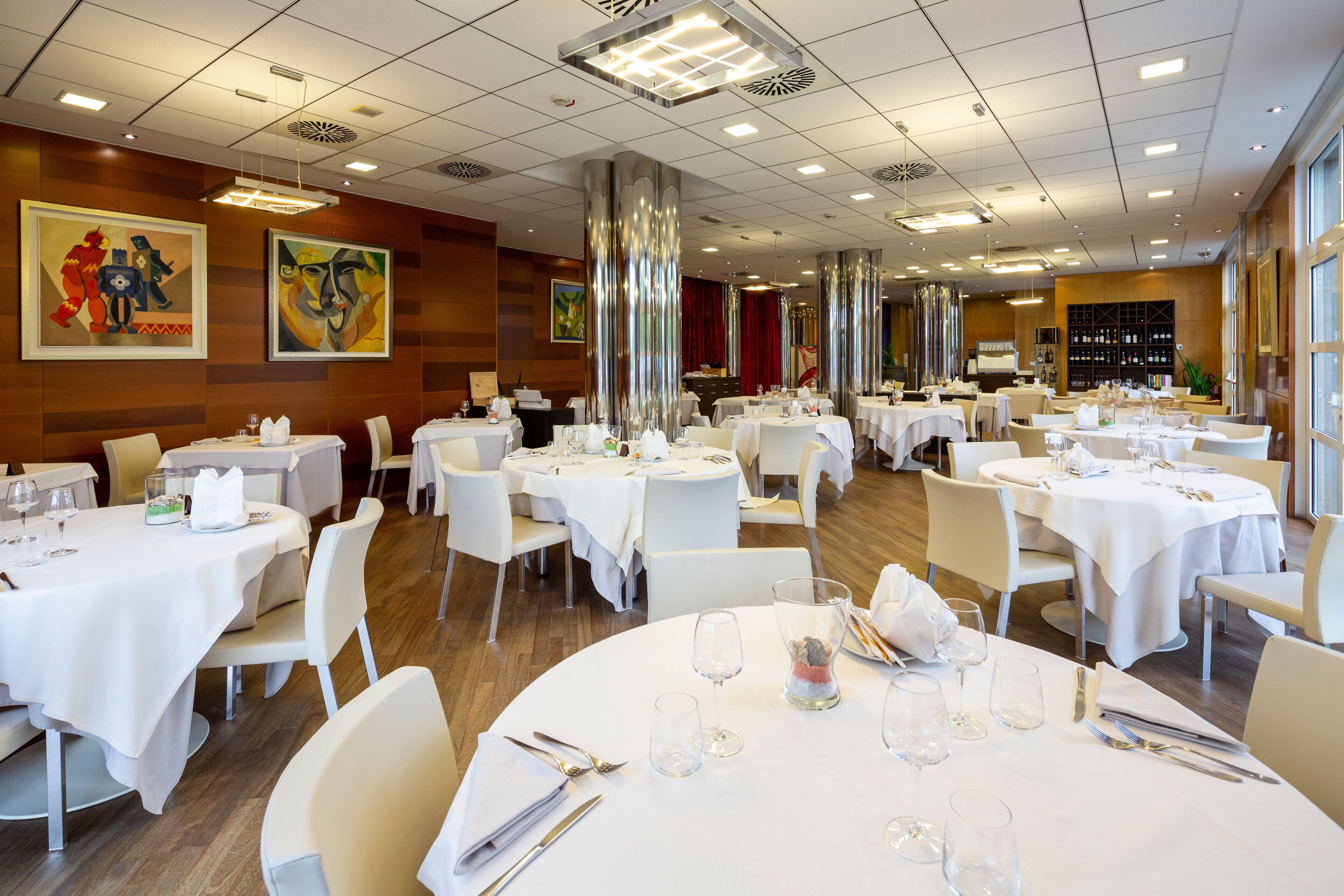 Un ristorante con tavoli rotondi, tovaglie bianche e diverse tipologie di posti a sedere.
