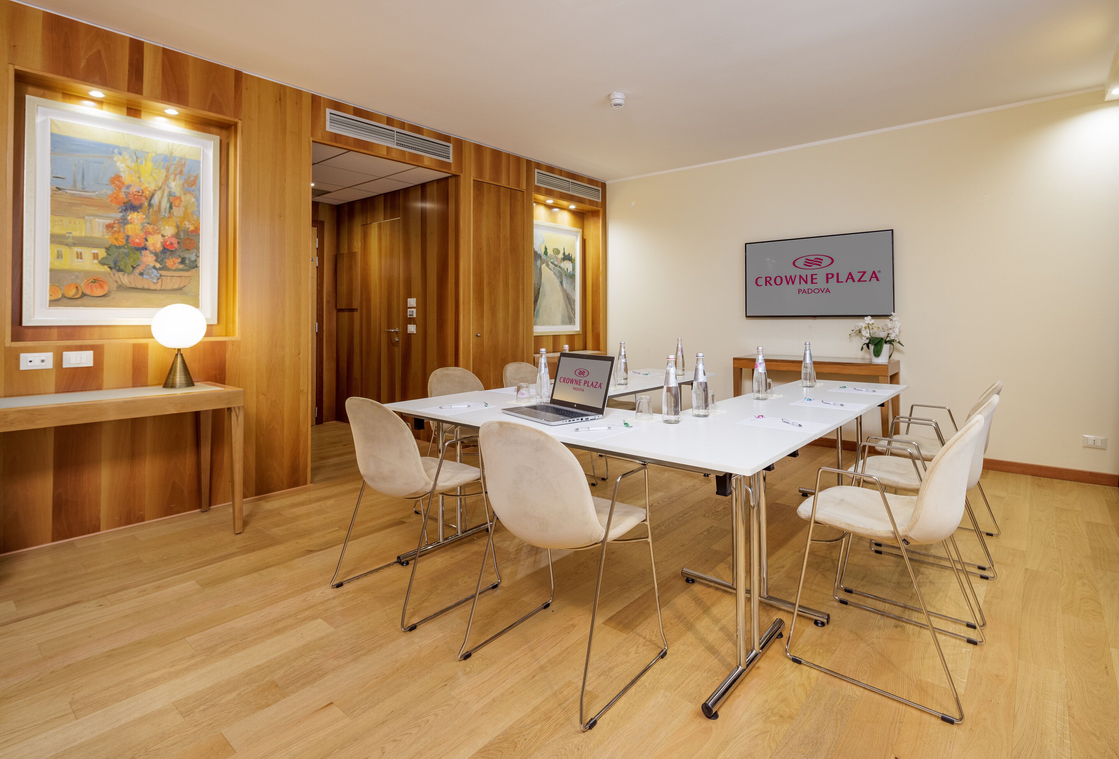 A conference room with a white table, six chairs, a laptop, water bottles, and a framed sign on the wall.