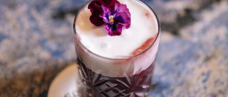 Un vaso con una bebida en capas y una flor morada encima, sobre un posavasos con texto.