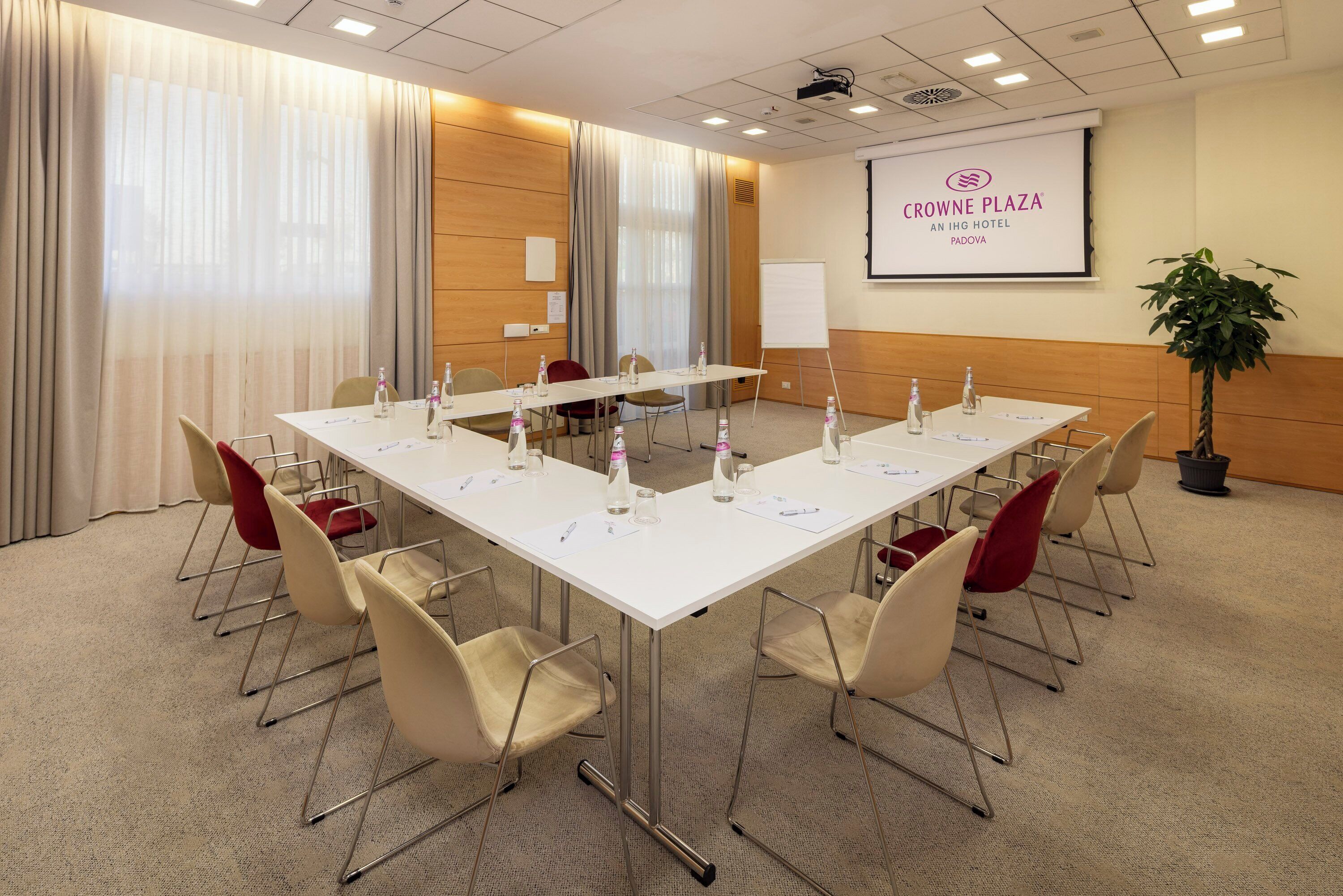 Un salón de conferencias con una larga mesa, sillas, una pantalla de proyector y una pizarra.