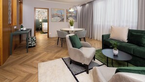 Una sala de estar moderna con un sofá verde, un sillón beige y una mesa de centro redonda. Hay una zona de comedor con una mesa pequeña y sillas, y un cuadro en la pared.