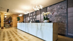 A reception desk with a marble top, a potted plant, and a cityscape mural on the wall. - Crowne Plaza Padova by IHG (Padova)