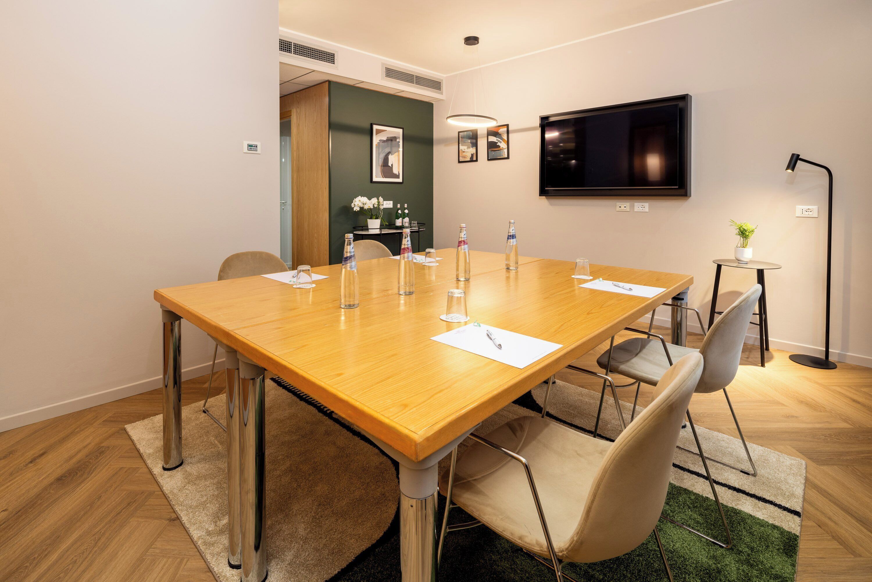 Un salón de conferencias con una mesa de madera, sillas, un televisor y una mesa pequeña con flores.