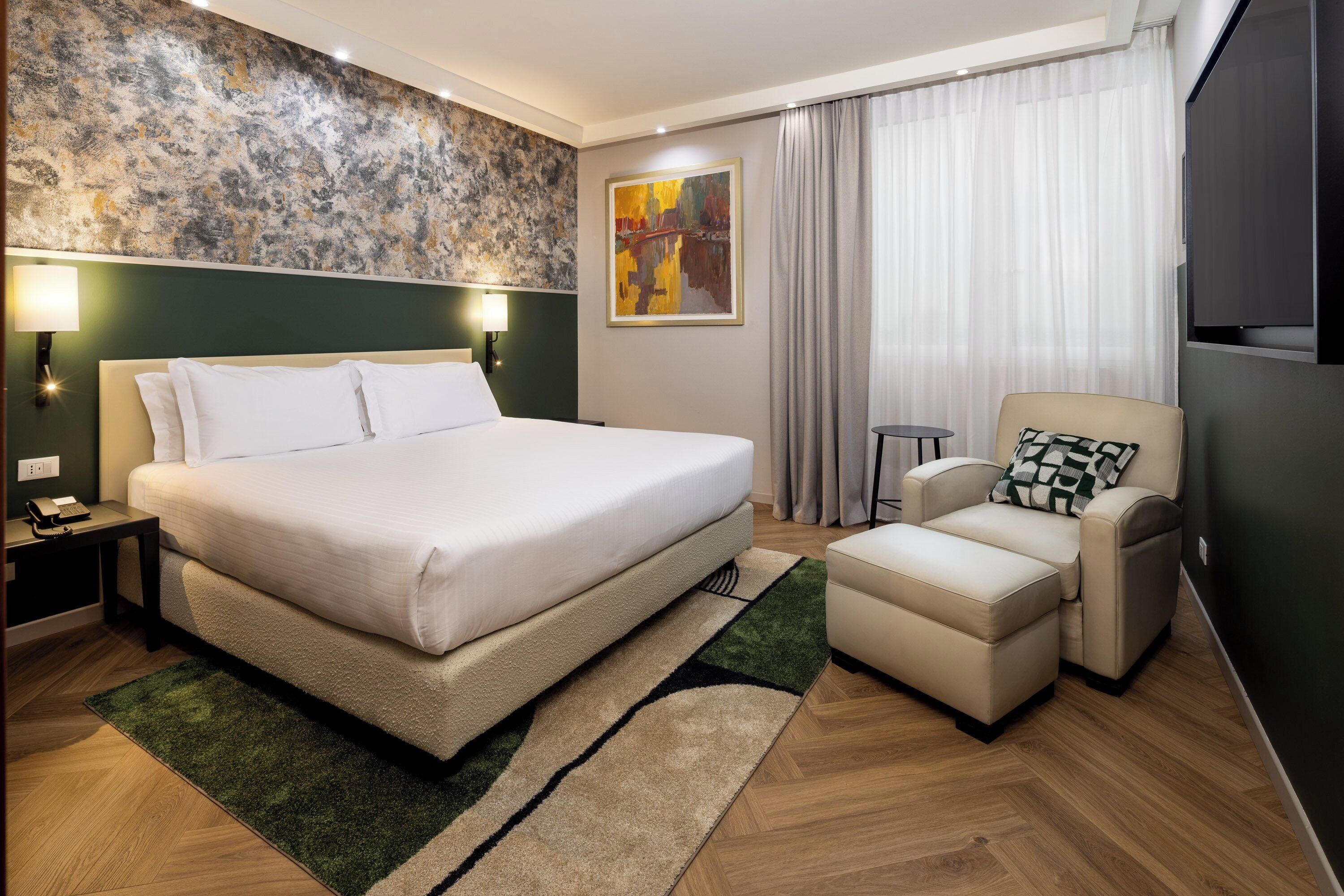 Une chambre d’hôtel avec un grand lit, une chaise, une petite table, un tableau au mur et un téléviseur.