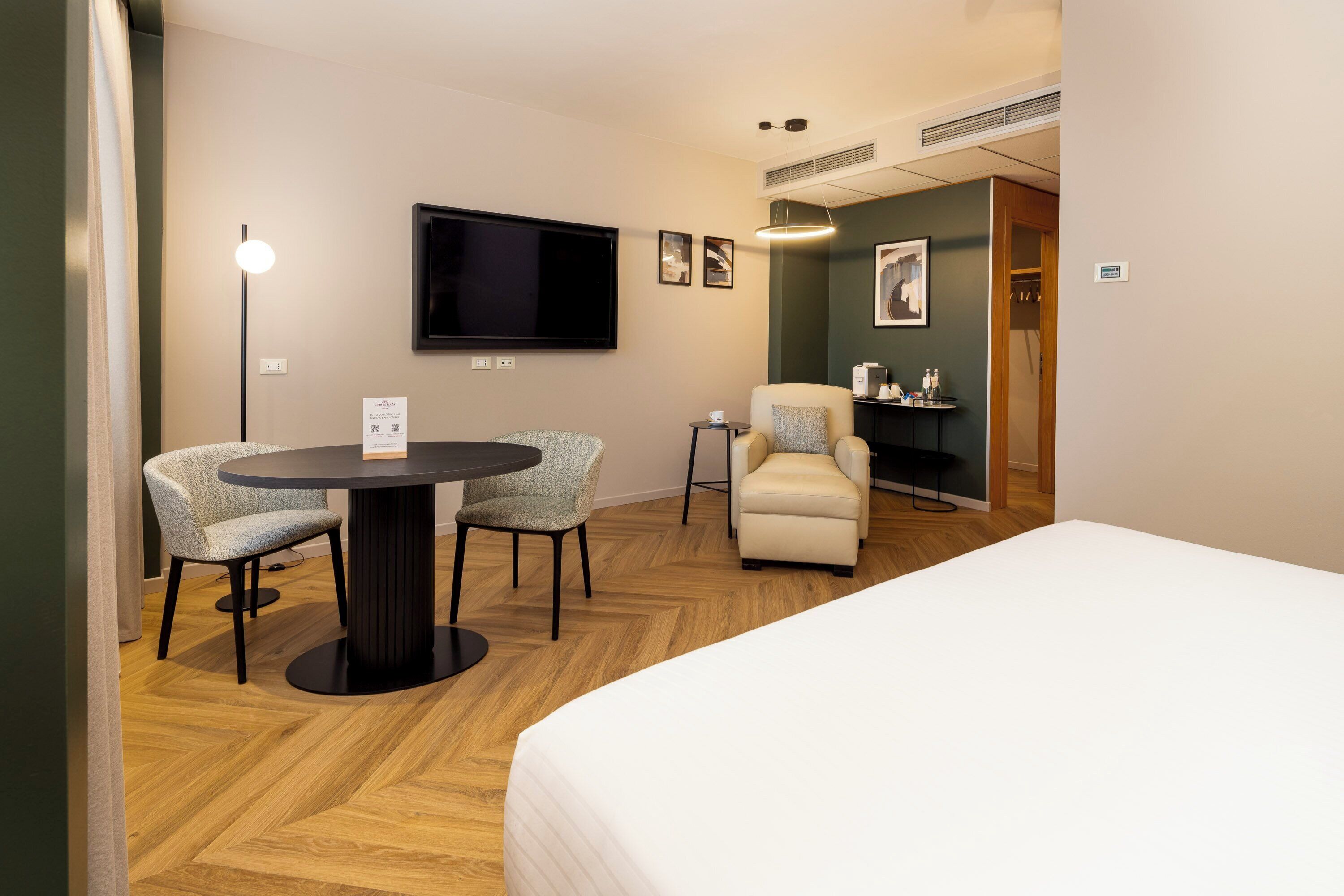 Habitación de hotel con cama, una mesa redonda con dos sillas, un televisor y una mesita de noche con lámpara.