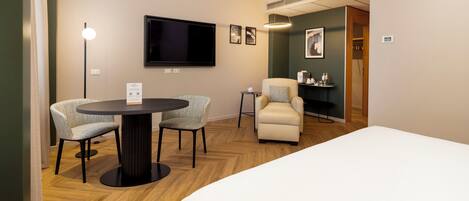 Habitación de hotel con cama, una mesa redonda con dos sillas, un televisor y una mesita de noche con lámpara.