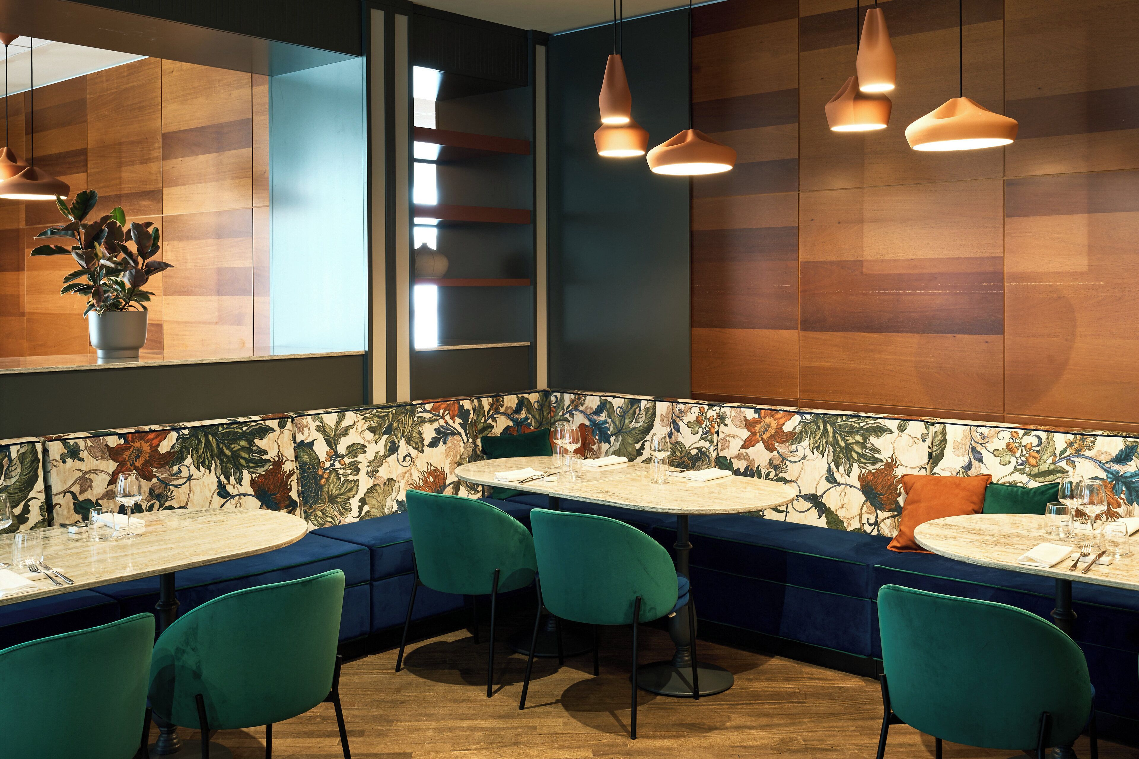 A restaurant with round tables, teal chairs, and a floral-patterned wall.