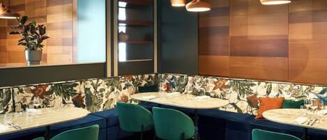 Um restaurante com mesas redondas, cadeiras cor de azul-esverdeado e uma parede com padrão floral.