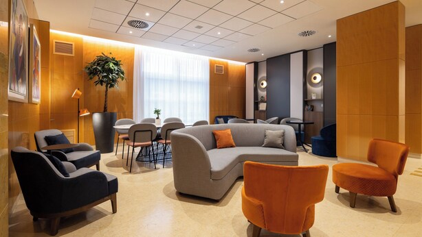 Un moderno vestíbulo de hotel con un amplio sofá modular, dos sillones, una mesita y una planta en maceta.