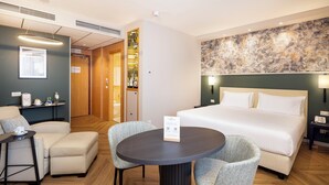 A hotel room with a bed, a round table with chairs, a small sofa, a coffee machine, and a wall-mounted artwork. - Crowne Plaza Padova by IHG (Padova)