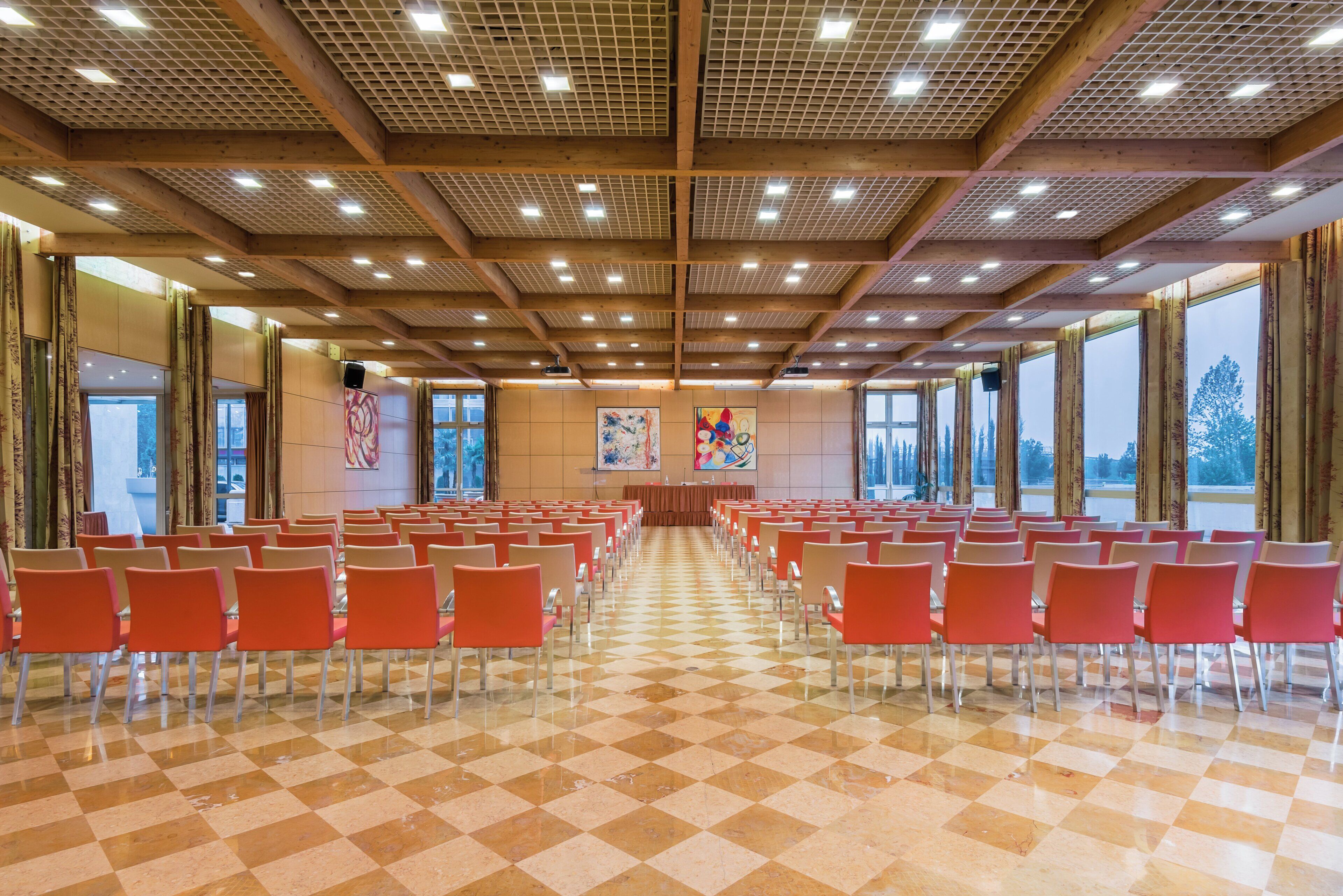 Un salón de conferencias con filas de sillas, un escenario con un atril y ventanas amplias.