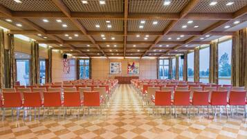 A conference room with rows of chairs, a stage with a podium, and large windows.