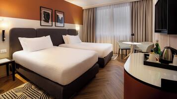 Een hotelkamer met twee bedden, een bureau, een stoel, een televisie en kunst aan de muur.