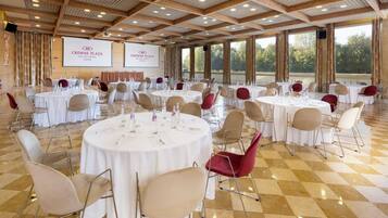 Ein Konferenzraum mit runden Tischen, beigen und roten Stühlen und einer großen Leinwand, die den Namen des Hotels zeigt.