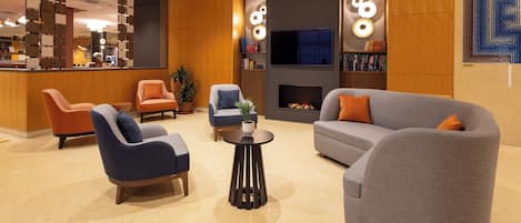 A modern lobby with seating, a fireplace, and a TV.
