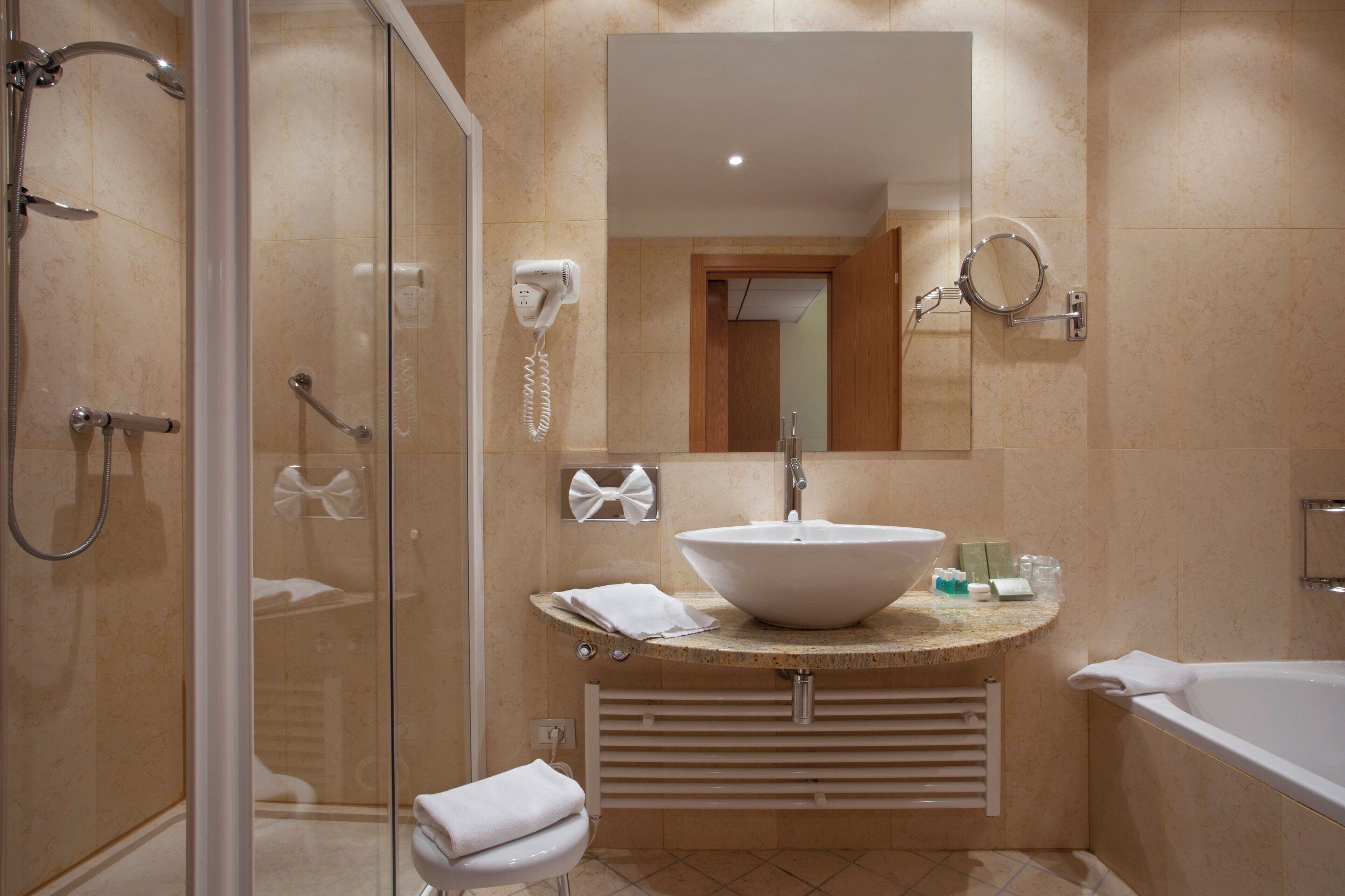 A modern bathroom with a glass shower enclosure, a large sink with a vessel basin, and a separate bathtub.