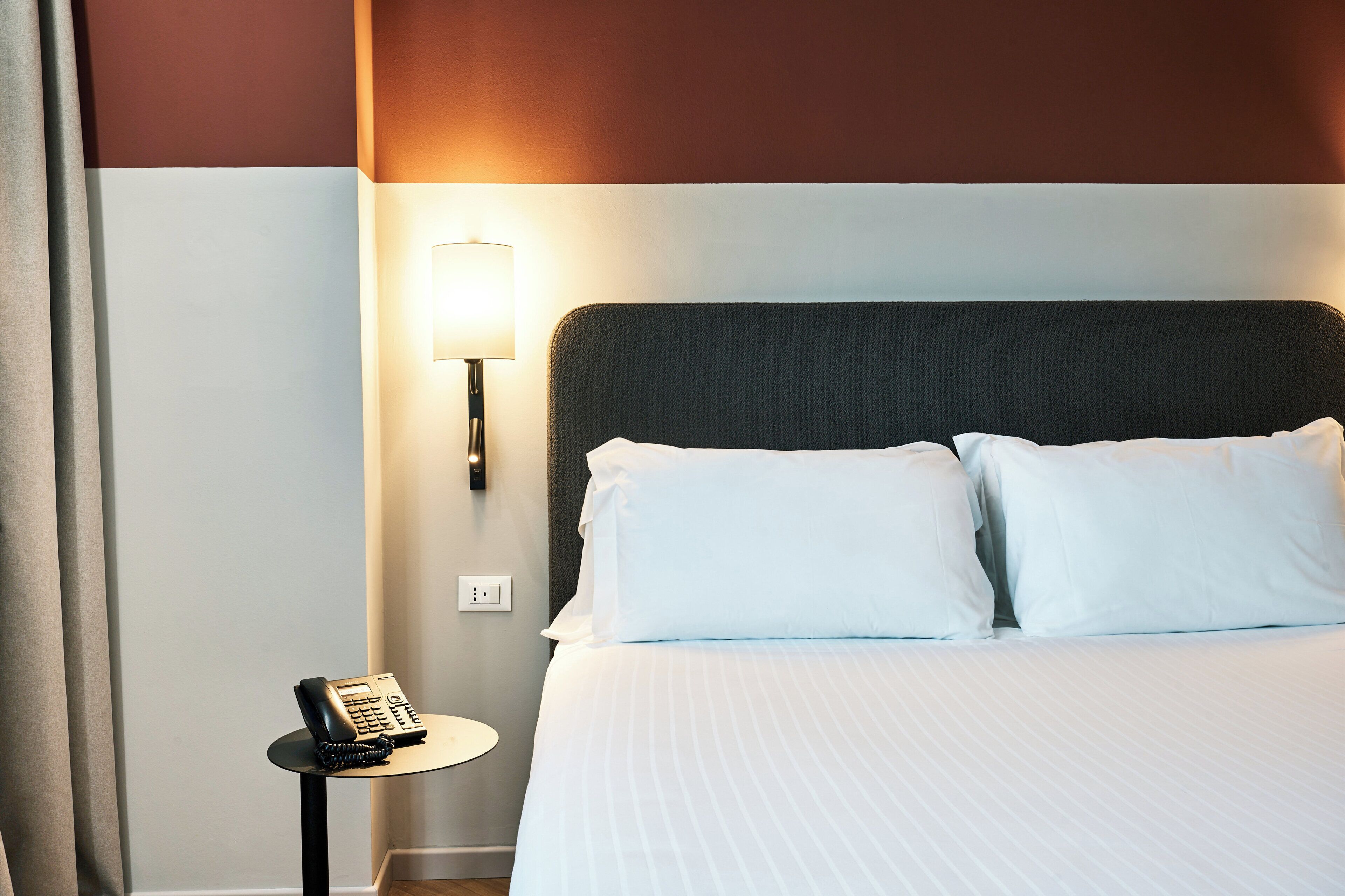 A neatly made bed with white linens, a bedside lamp, and a telephone on a small table beside it.