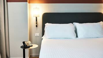 A neatly made bed with white linens, a bedside lamp, and a telephone on a small table beside it.