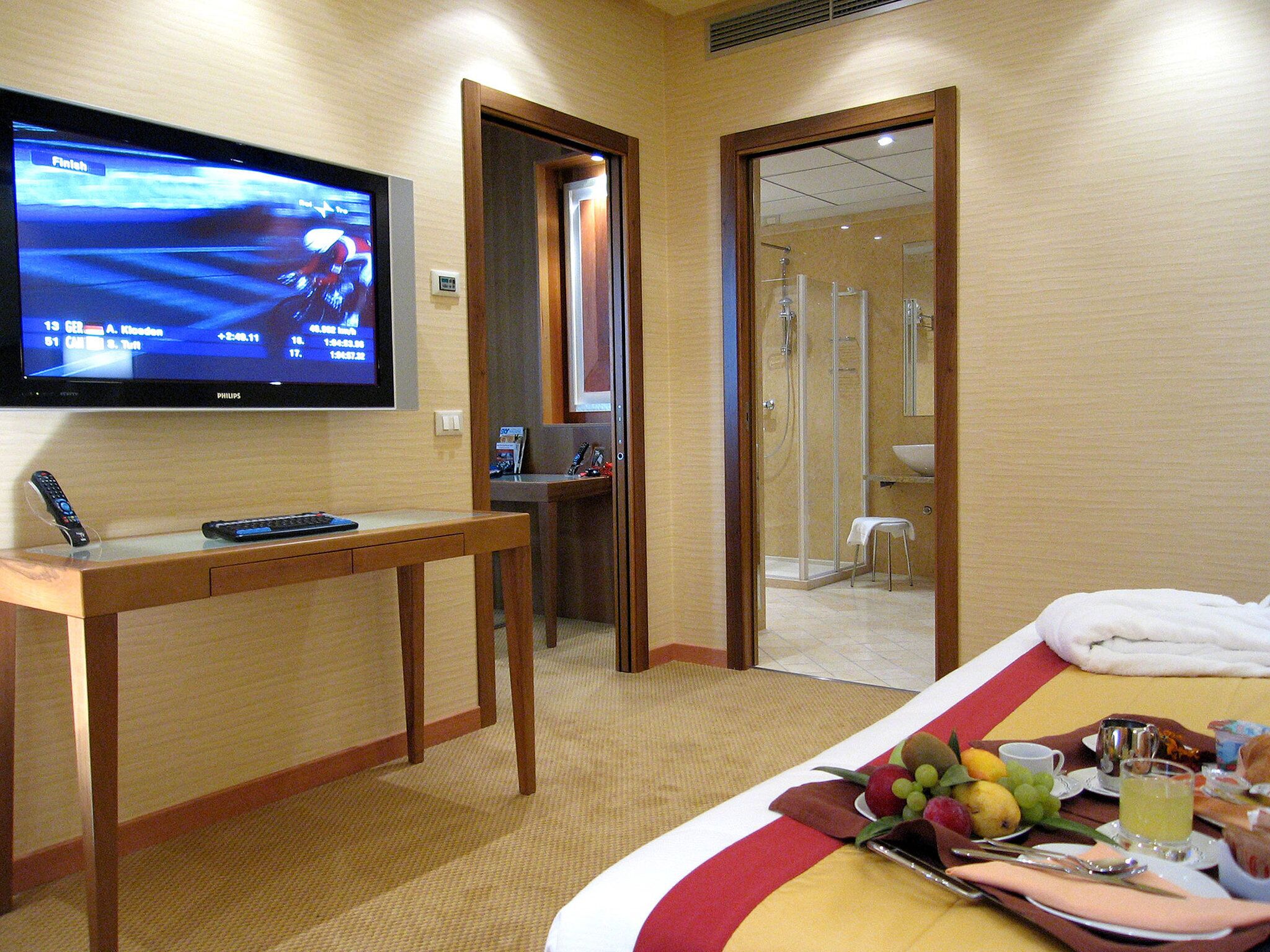 A hotel room with a television, a desk, a bed with a red and white striped bedspread, and a fruit basket.