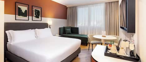 Una habitación de hotel con una cama grande, un escritorio con una silla, una mesita y un televisor.