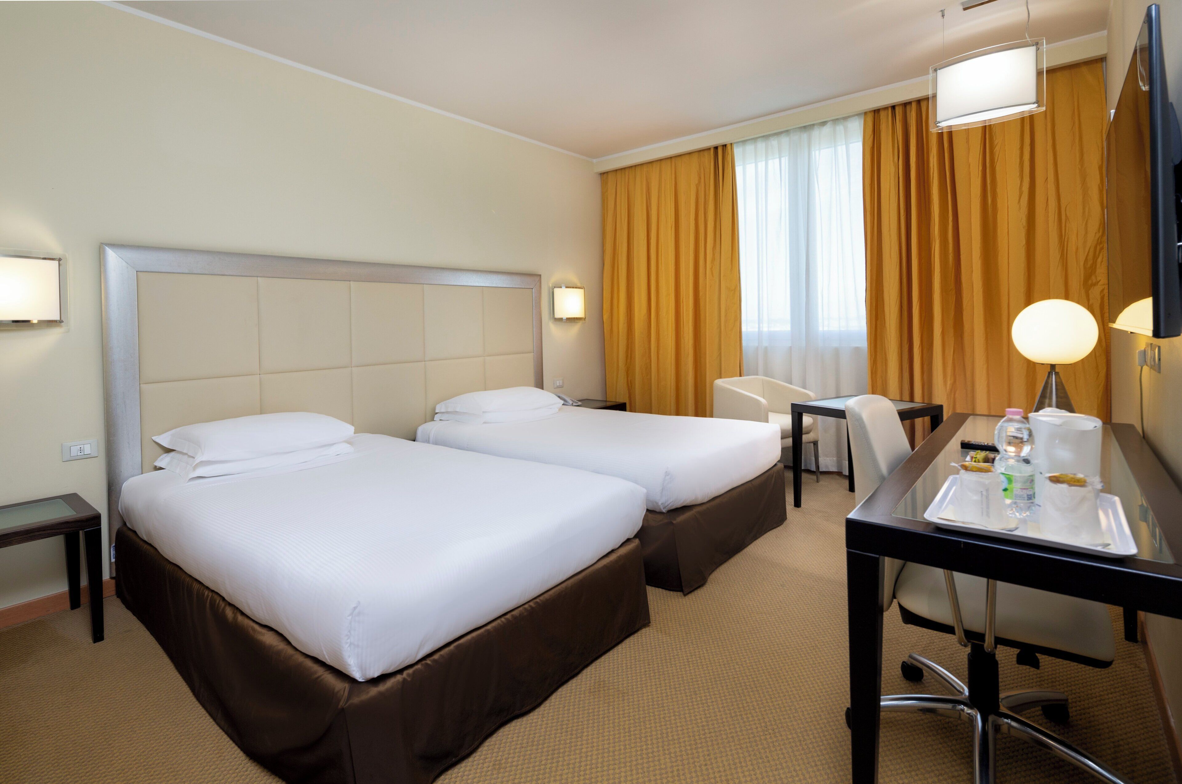 A hotel room with two beds, a desk with a tray of breakfast items, a chair, and a large mirror.