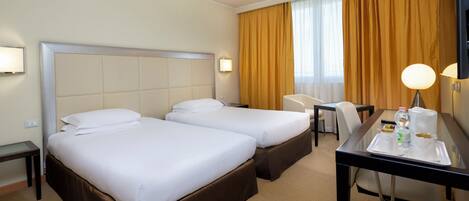A hotel room with two beds, a desk with a tray of breakfast items, a chair, and a large mirror.
