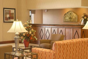 Área de recepção de hotel com sofá, cadeiras, balcão, luminária, arranjo de flores e um letreiro com a inscrição 'WINGATE BY WYNDHAM'.