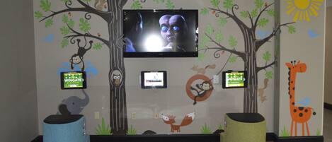 Un área de juegos infantiles con televisor, adornos en la pared y dos grandes pufs.