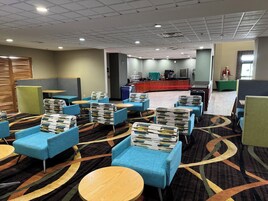 Vestíbulo de hotel con sillones azules, una mesa de recepción y una estación de café.