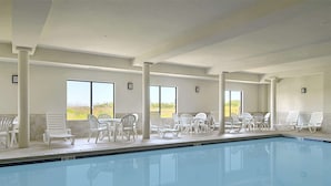 A pool area with white lounge chairs and tables, large windows, and a clear view of the outdoors. - Wingate by Wyndham Warner Robins (Warner Robins)