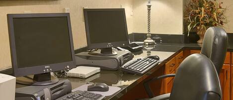 Un bureau d’hôtel équipé de deux écrans, d’un bureau, d’un clavier, d’une souris, d’une lampe et d’une chaise.