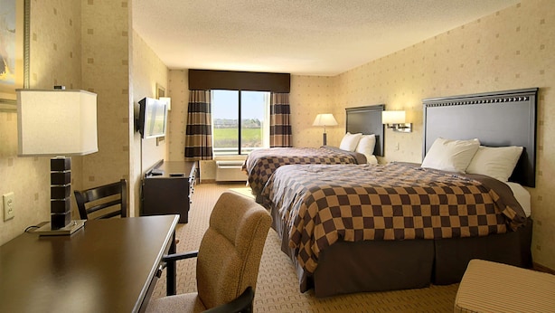A hotel room with two beds, a desk, a chair, a TV, and a window with curtains. - Wingate by Wyndham Warner Robins (Warner Robins)