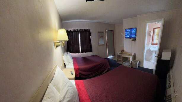 A hotel room with a large bed, a bedside table, a lamp, a TV, and a bathroom visible through an open door.