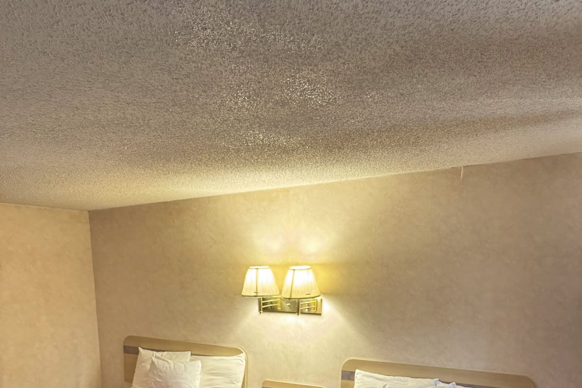A hotel room with two beds, each with a red bedspread, a nightstand with a lamp, and a wall-mounted light fixture.