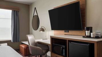 A hotel room with a bed, a desk with a chair, a television, a microwave, a coffee maker, and a small refrigerator.