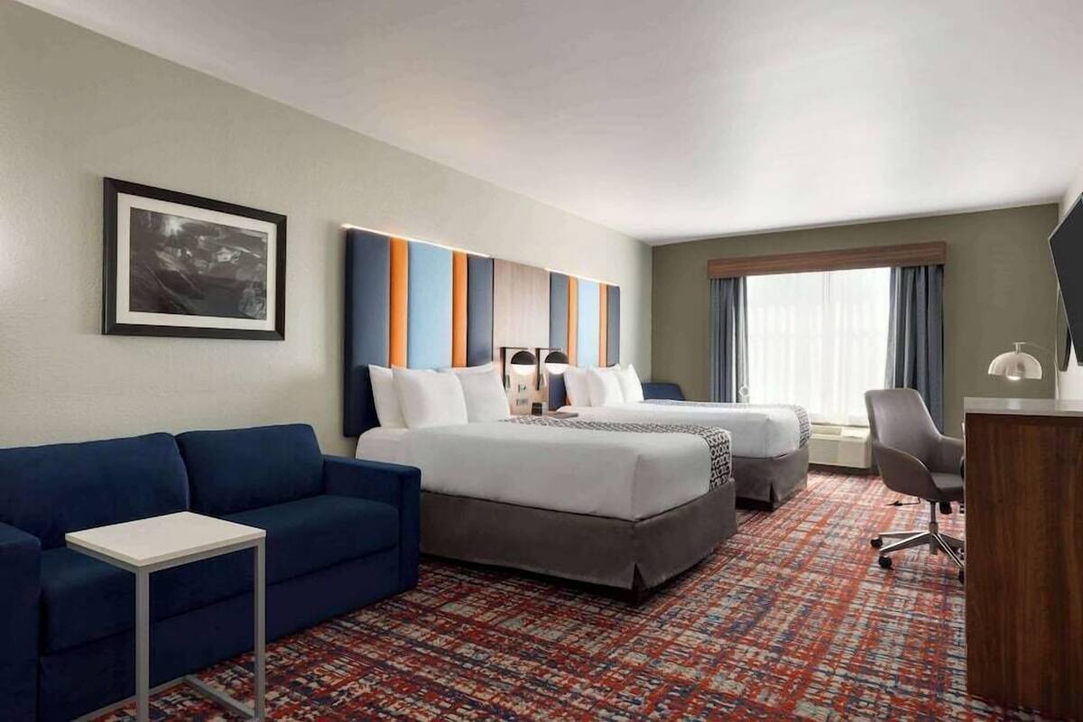 Une chambre d’hôtel avec un lit, deux tables de chevet, un canapé, un bureau et une grande fenêtre.