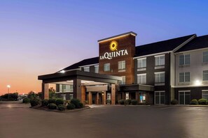 Un hotel con un llamativo letrero de 'La Quinta', un acceso cubierto y un estacionamiento.